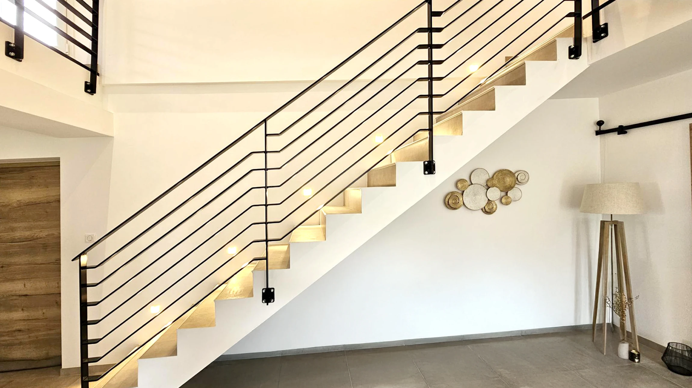 Porte de garage sectionnelle grise anthracite installée sur façade moderne beige avec murs en béton