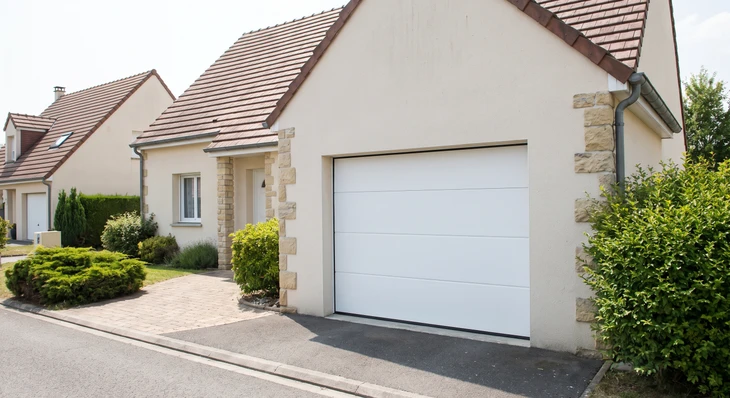 Porte de garage en acier massif renforcé, installée sur la façade d'un garage attenant à une maison résidentielle, avec des gonds et serrures apparentes de haute sécurité, panneaux métalliques épais et design robuste, sous l'éclairage naturel mettant en avant son aspect solide et fiable.
