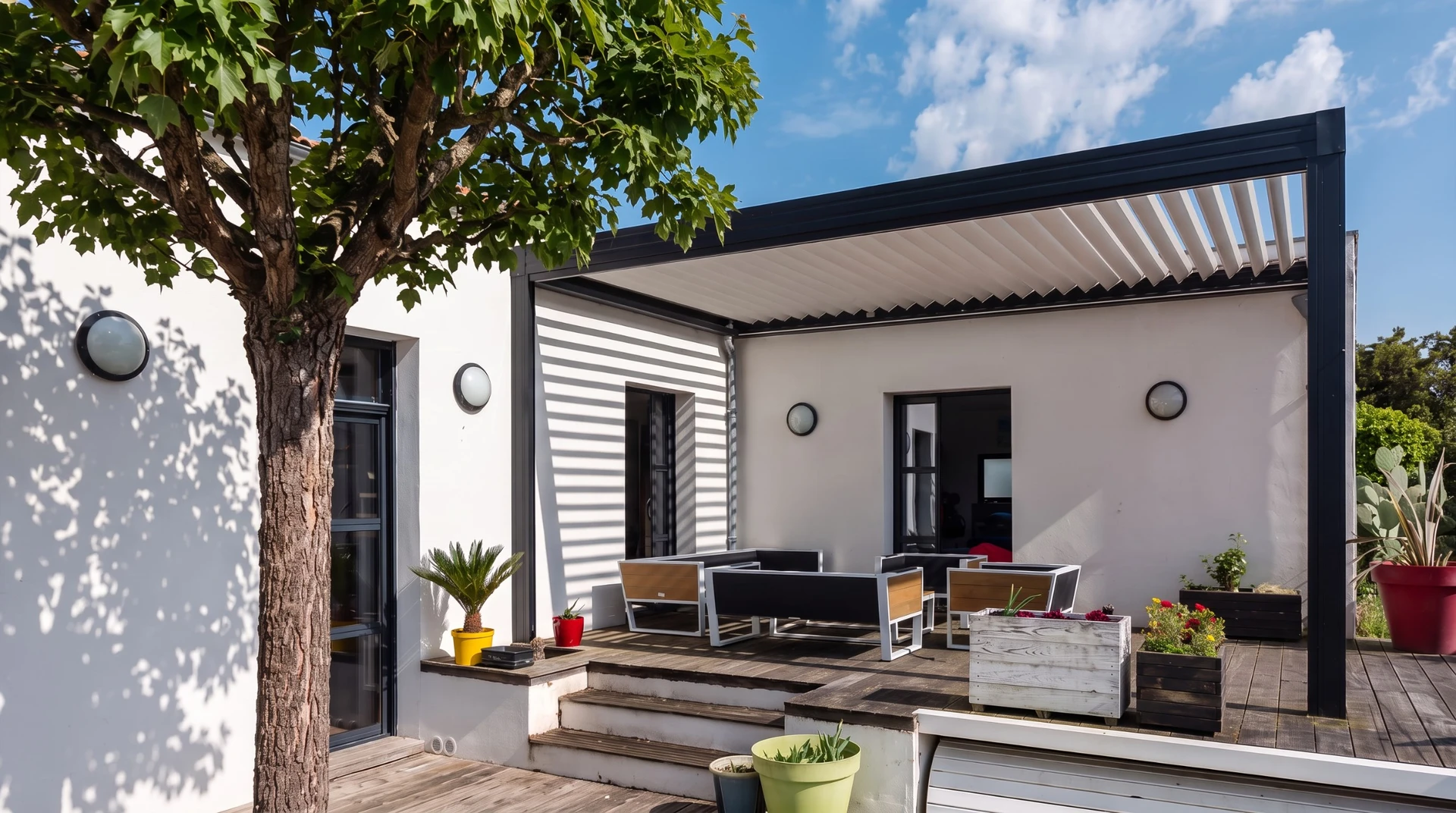 Terrasse extérieure moderne avec salon de jardin en bois et coussins gris sous pergola bioclimatique à lames orientables