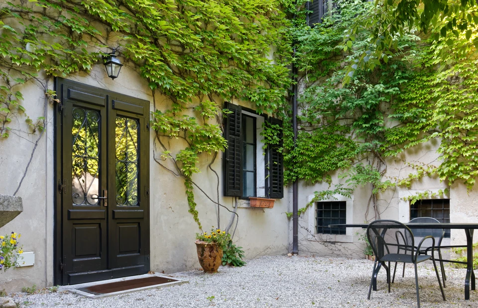 Façade extérieure d'une maison résidentielle avec un volet en aluminium gris fixé sur mesure sur une fenêtre, en position fermée, montrant les charnières de qualité professionnelle et l'intégration harmonieuse avec l'architecture de la façade en pierre ou crépi. La pose récente met en évidence la robustesse et l'isolation thermique de l'équipement.