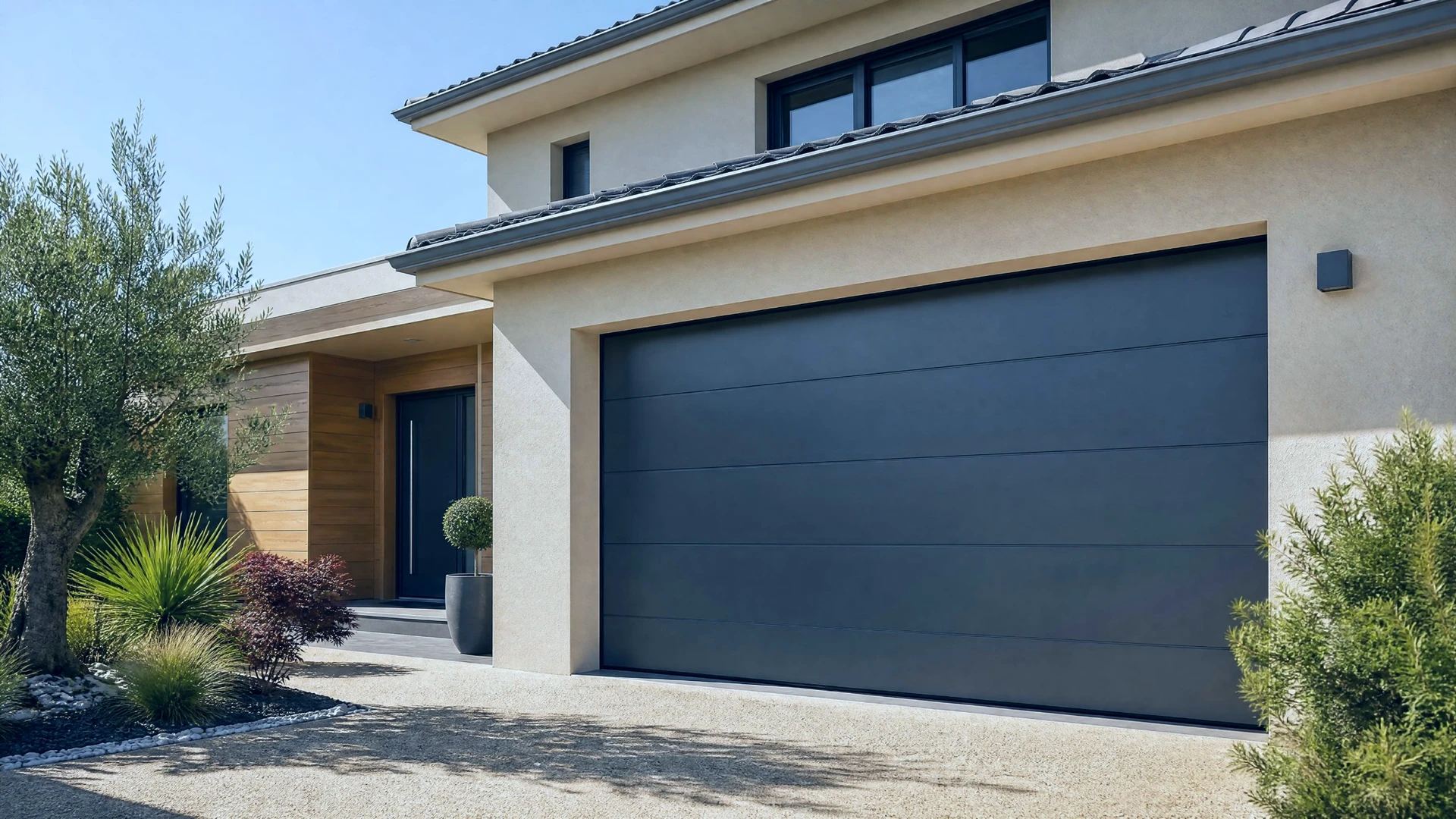 Porte de garage sectionnelle grise anthracite installée sur façade moderne beige avec murs en béton